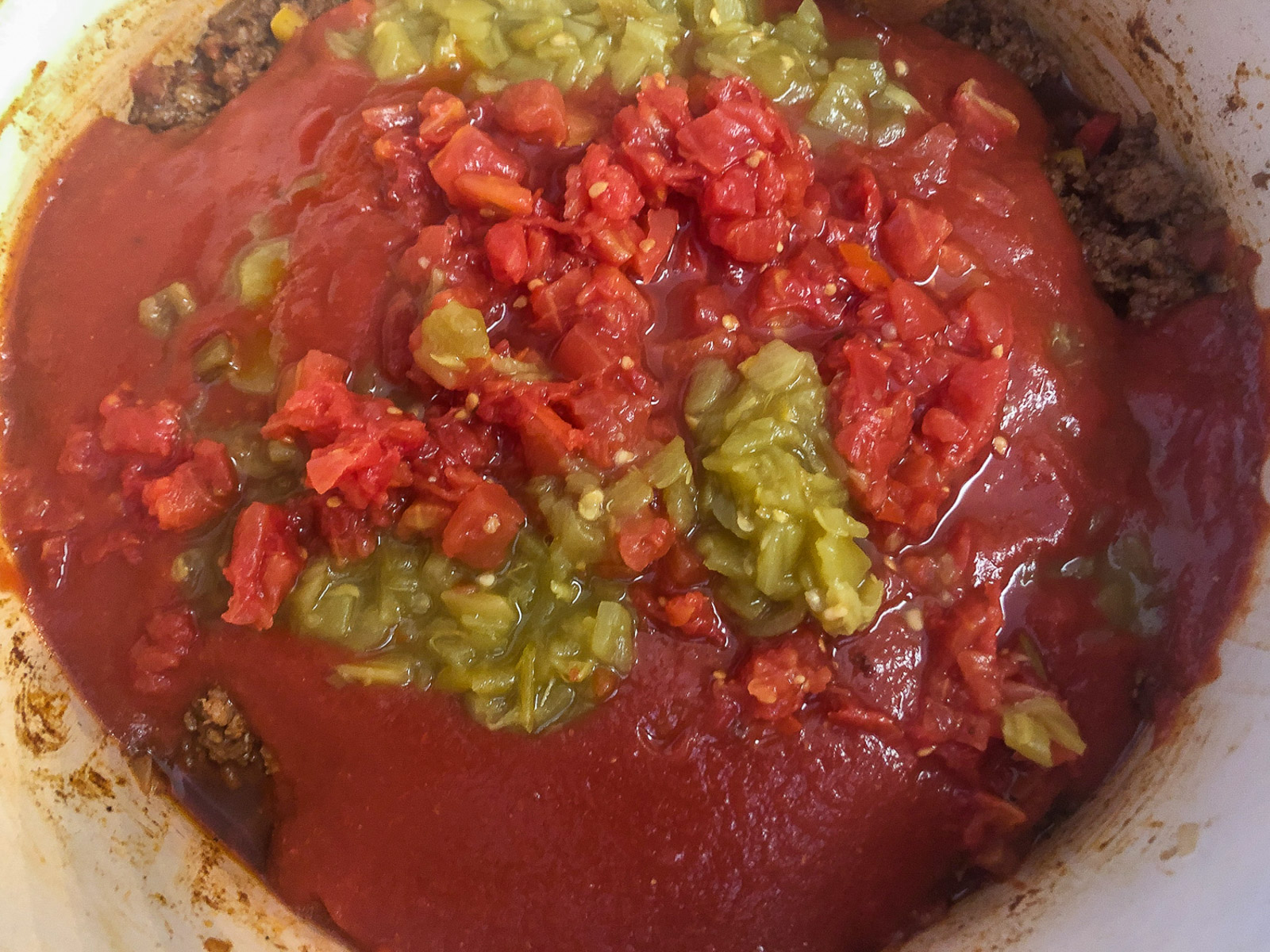 Tomato sauce, diced tomatoes, and green chiles poured over seasoned sausage and vegetables in a Dutch oven.