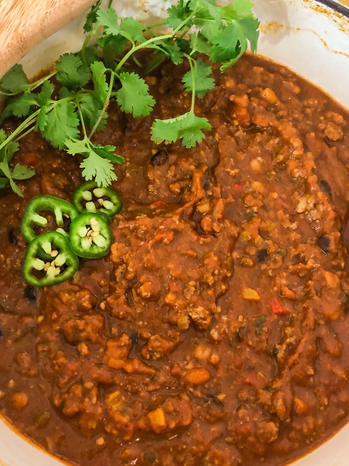 Close-up of finished pumpkin chili in the Dutch oven garnished with fresh cilantro and sliced jalapeños.