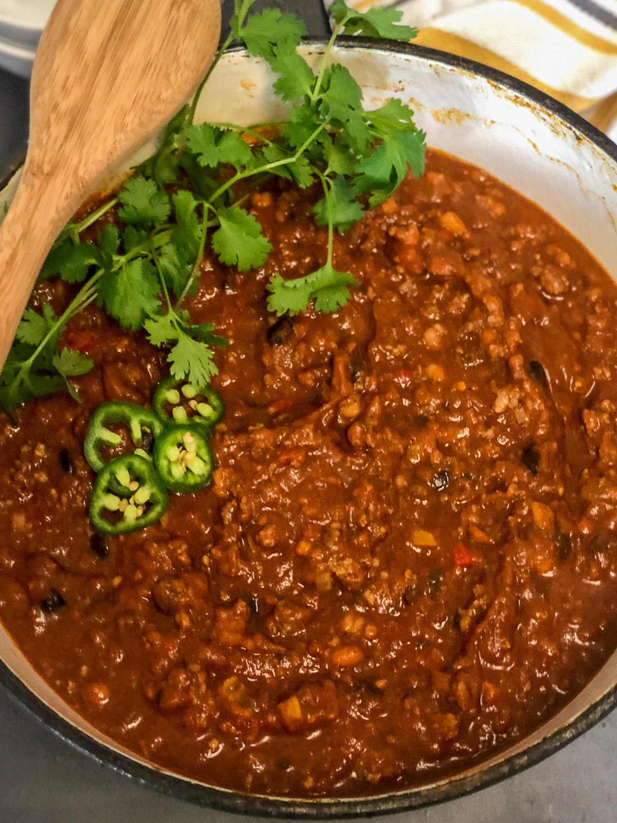 Dutch oven pumpkin chili garnished with fresh cilantro, jalapeño slices, and a wooden spoon.