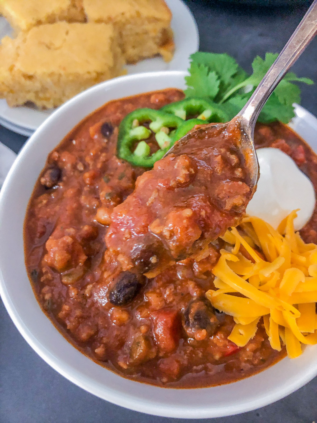 Close-up of a spoonful of pumpkin chili in a white bowl with sour cream, jalapeños, and shredded cheddar cheese.