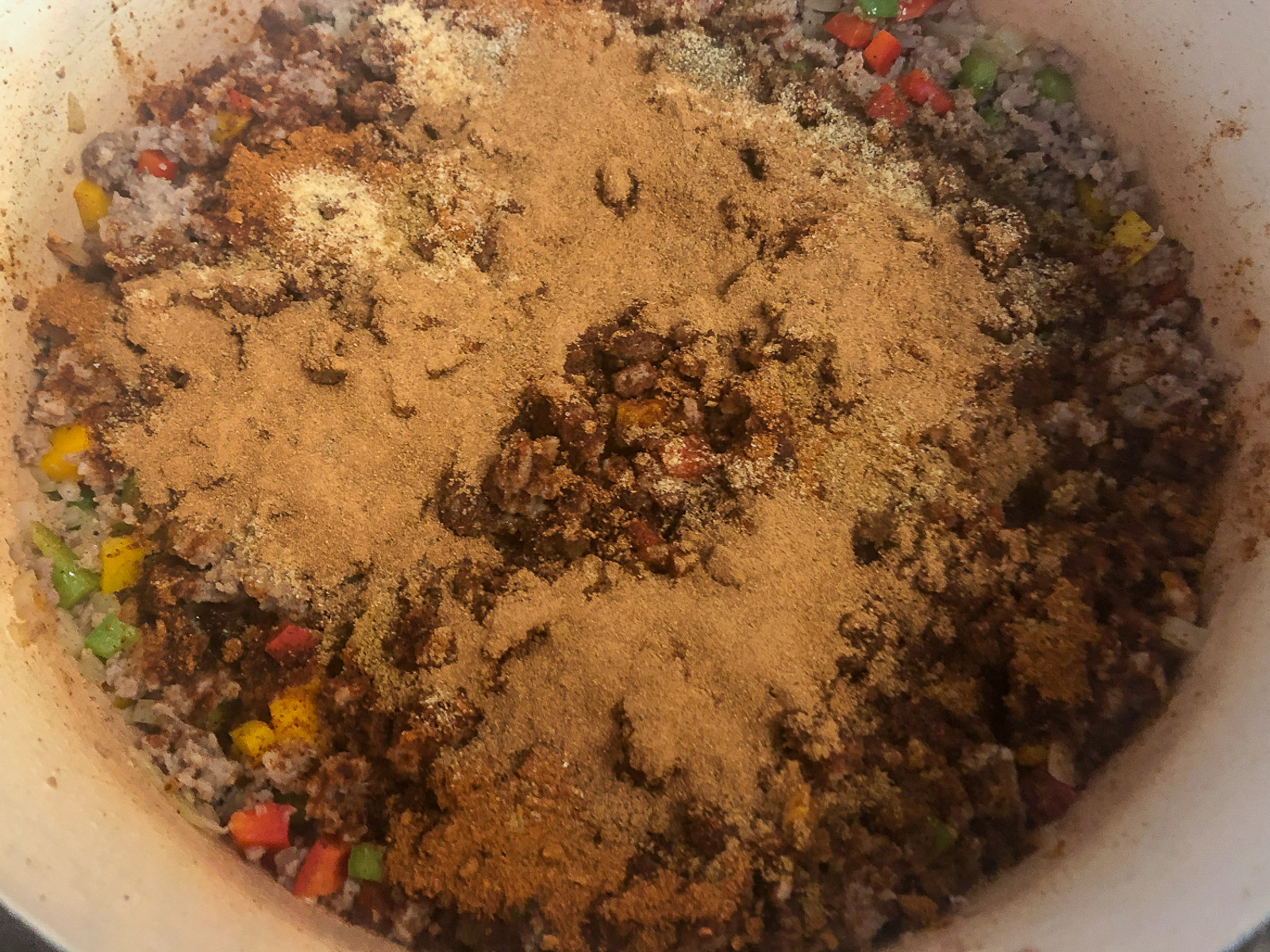 Chili mix, pumpkin pie spice, cumin, garlic, salt, and pepper sprinkled over the cooked sausage and vegetables in the Dutch oven.