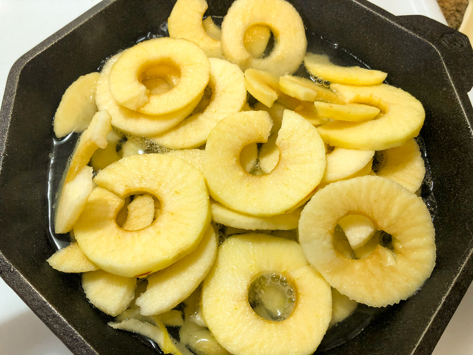 Sliced apples simmering in water inside a black cast iron skillet