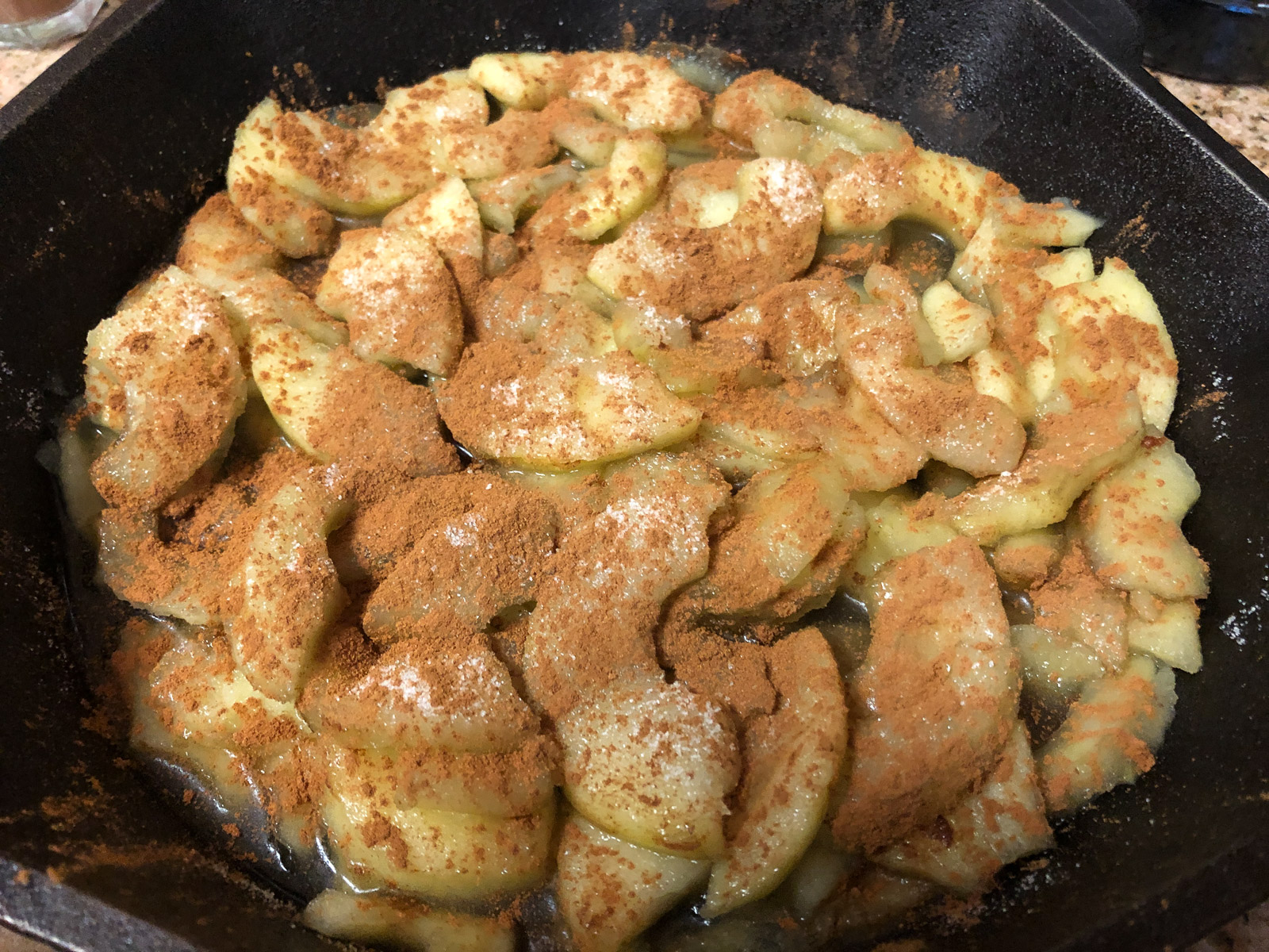 Drained apple slices coated with sugar and cinnamon in a black cast iron skillet