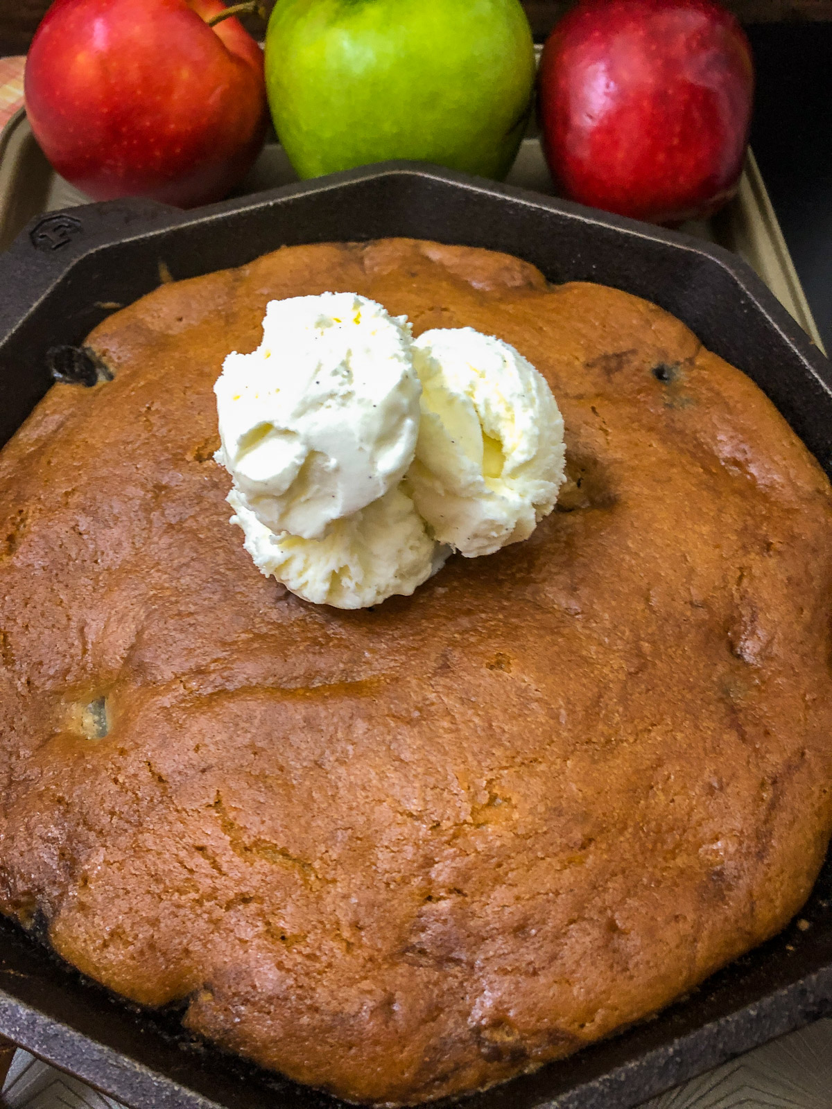 Dutch oven apple cake baked in a cast iron skillet topped with a scoop of vanilla ice cream