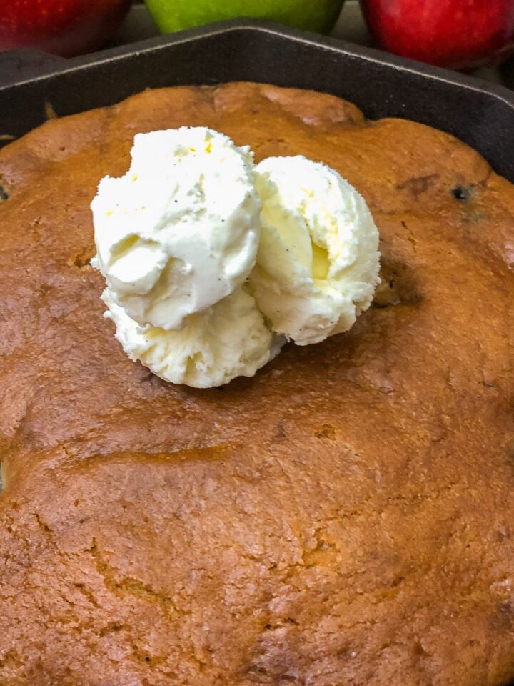 Dutch oven apple cake in a cast iron skillet with vanilla ice cream and fresh apples in background
