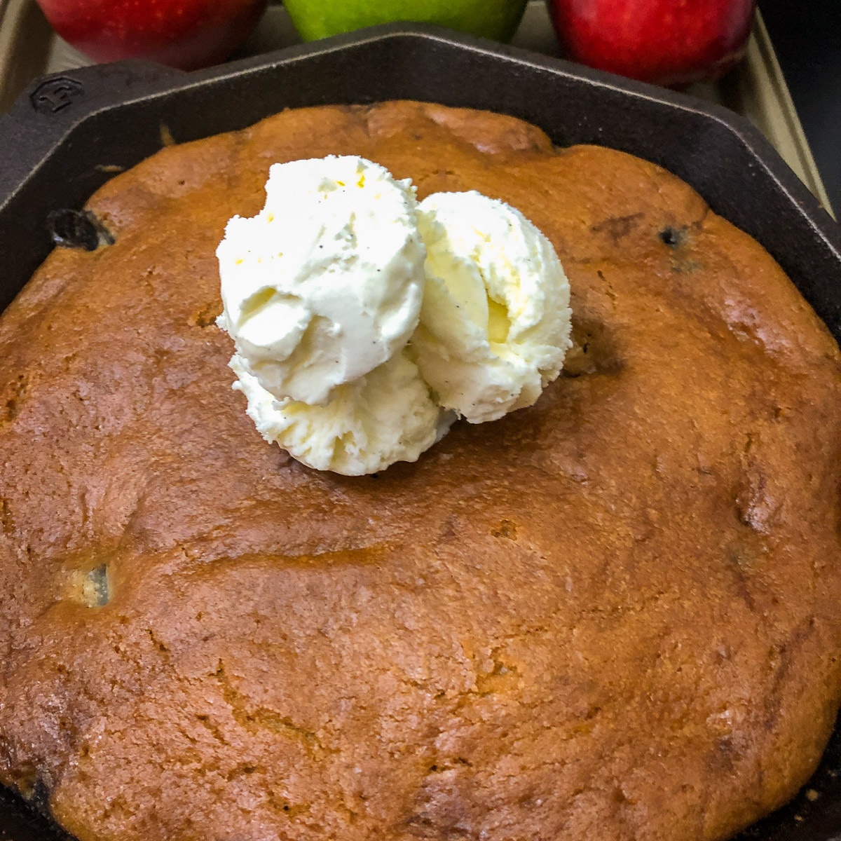 Dutch oven apple cake in a cast iron skillet with vanilla ice cream and fresh apples in background