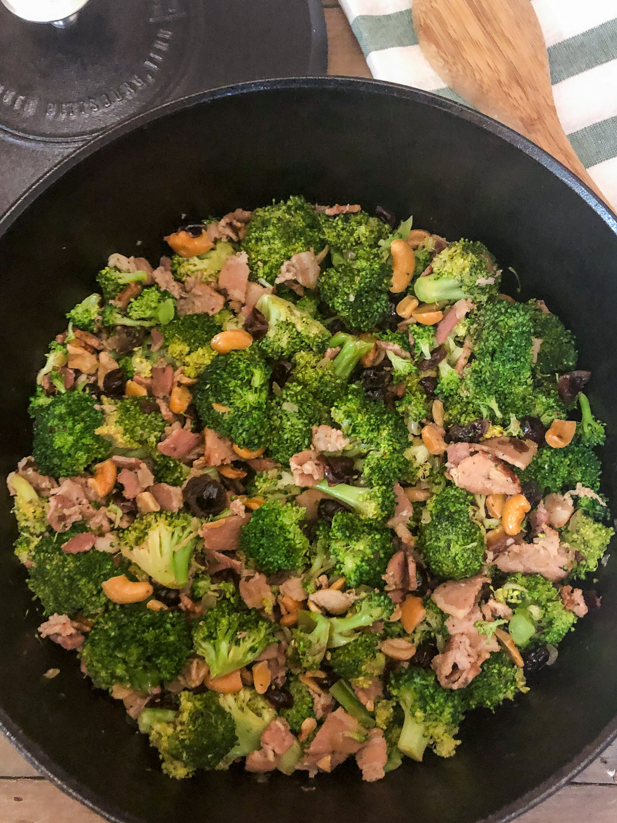 Finished cranberry broccoli salad shown in the cast iron Dutch oven with lid and wooden spoon