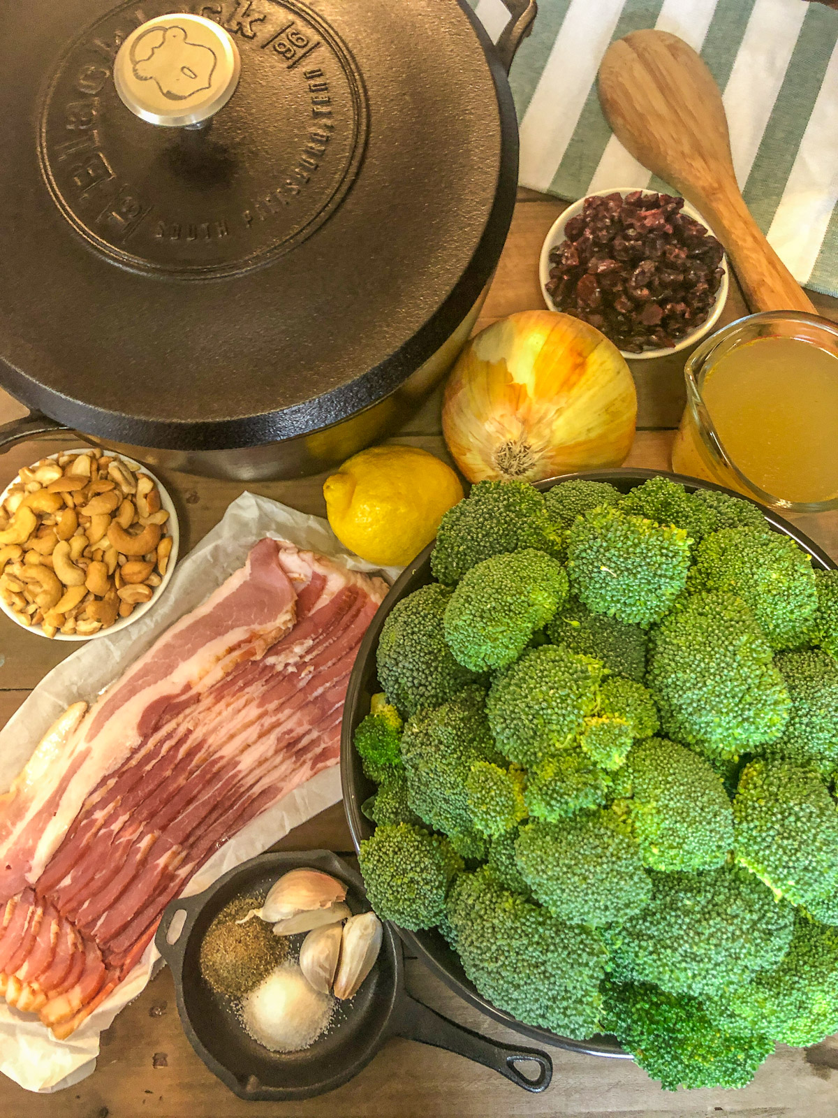 Ingredients for broccoli cranberry salad: bacon, broccoli, dried cranberries, cashews, lemon, onion, broth, and seasonings with a cast iron Dutch oven
