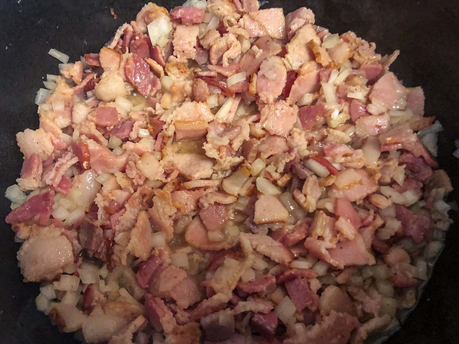 Chopped bacon and diced onions cooking in a cast iron Dutch oven