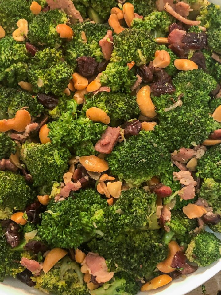 Cranberry broccoli salad with bacon and cashews in a white bowl, overhead view with cast iron Dutch oven