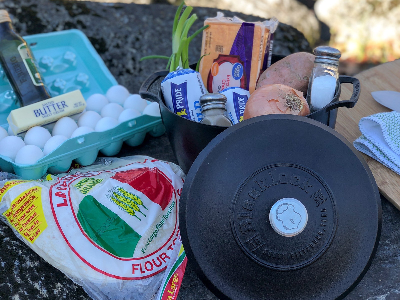 Mountain man breakfast ingredients laid out: sweet potatoes, sausage, eggs, cheese, and green onions.