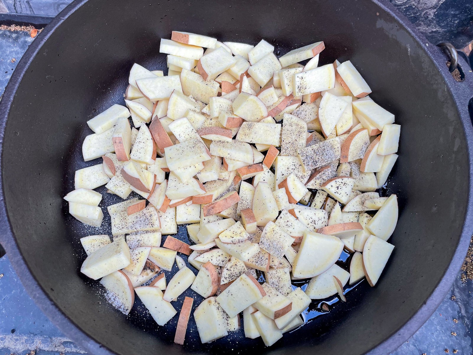 Seasoned sweet potatoes and onions cooking in a Dutch oven.