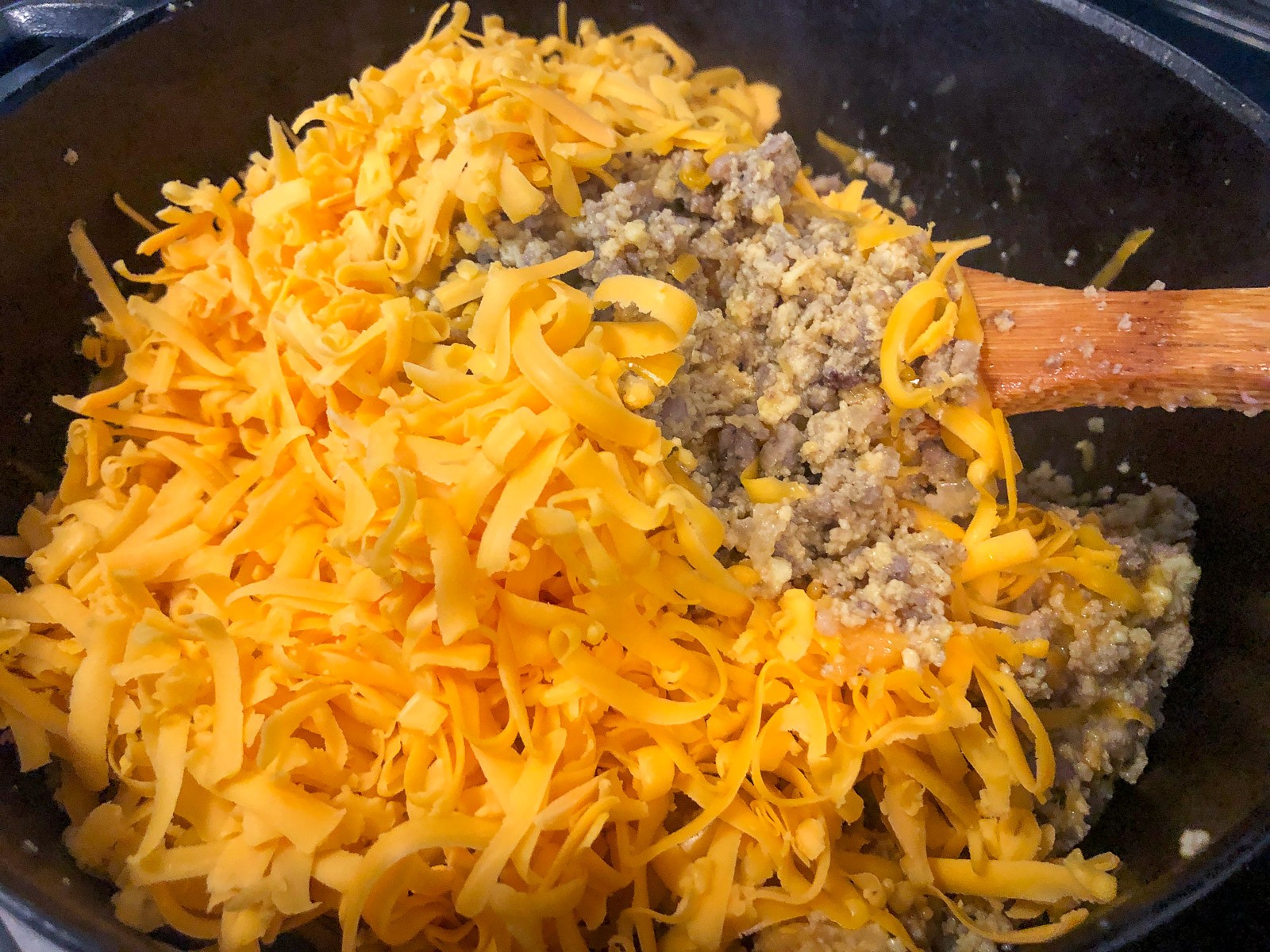 Shredded cheddar cheese being stirred into the mountain man breakfast casserole.