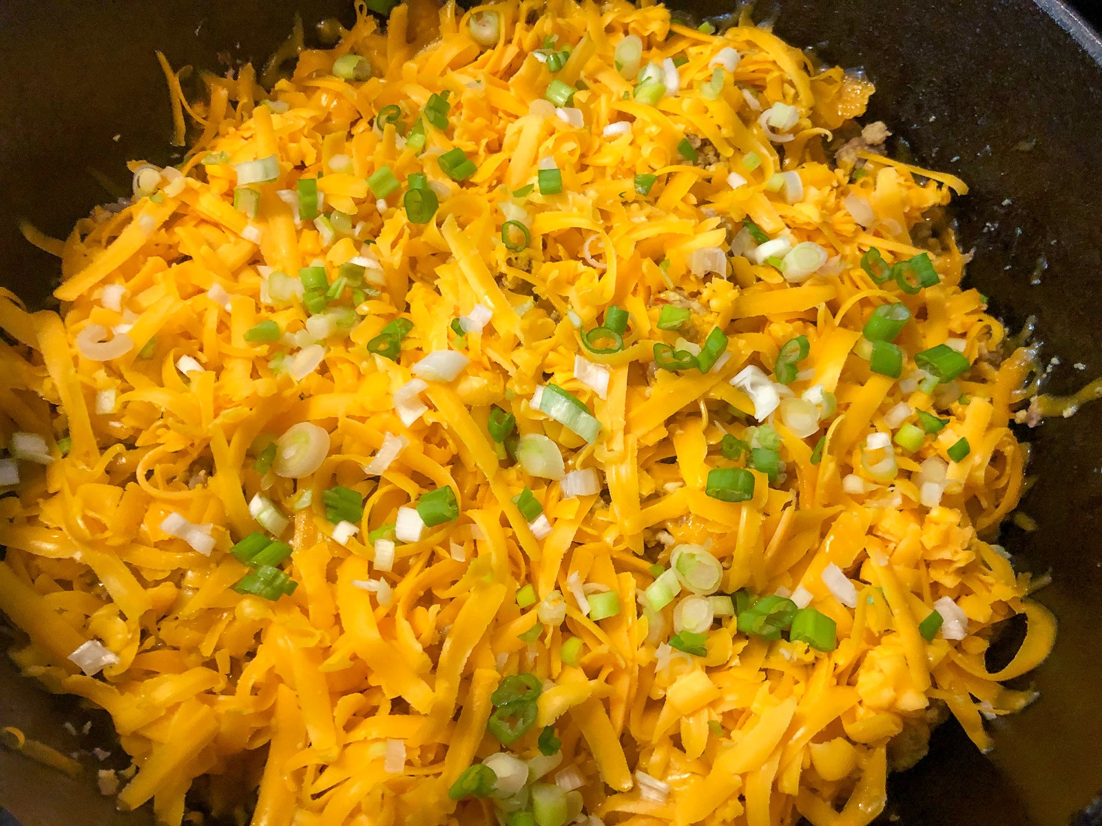 Melted cheese and green onions topping the finished mountain man breakfast.