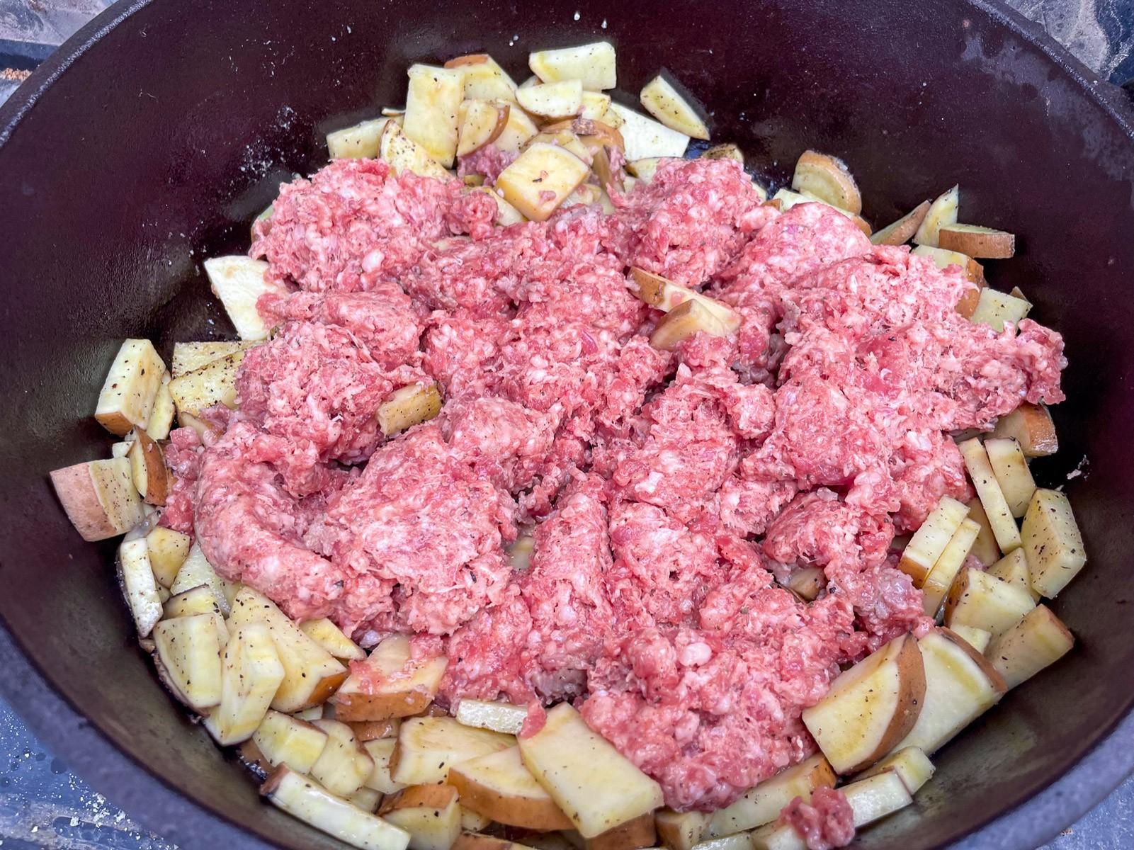 Raw ground sausage crumbled over sweet potatoes in the Dutch oven.