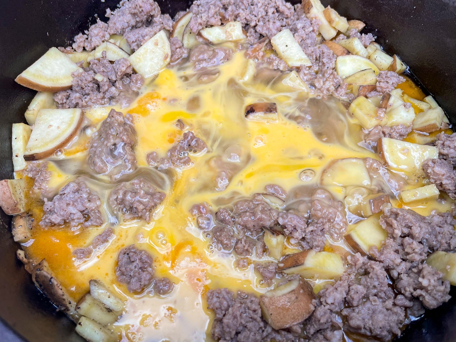 Beaten eggs poured over sausage and sweet potatoes in the Dutch oven.
