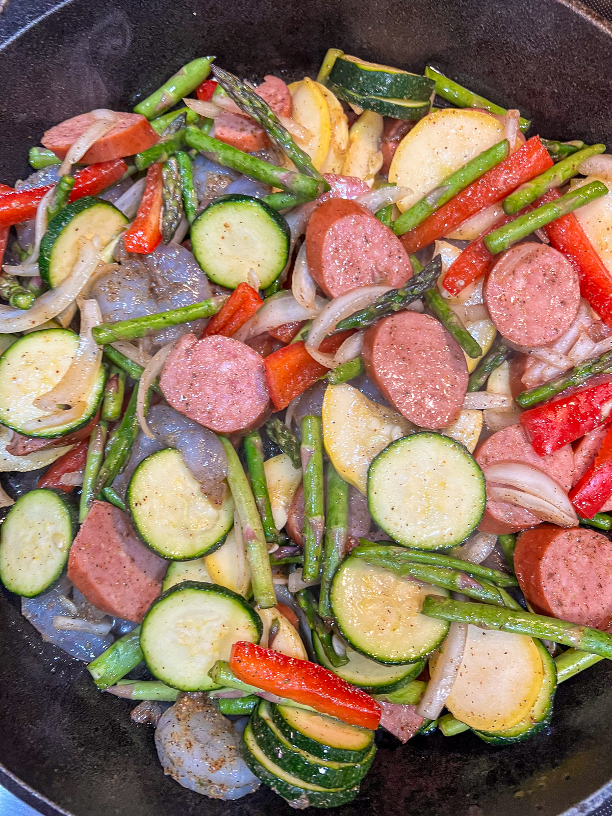 Shrimp and sausage cooking in a skillet with vegetables.
