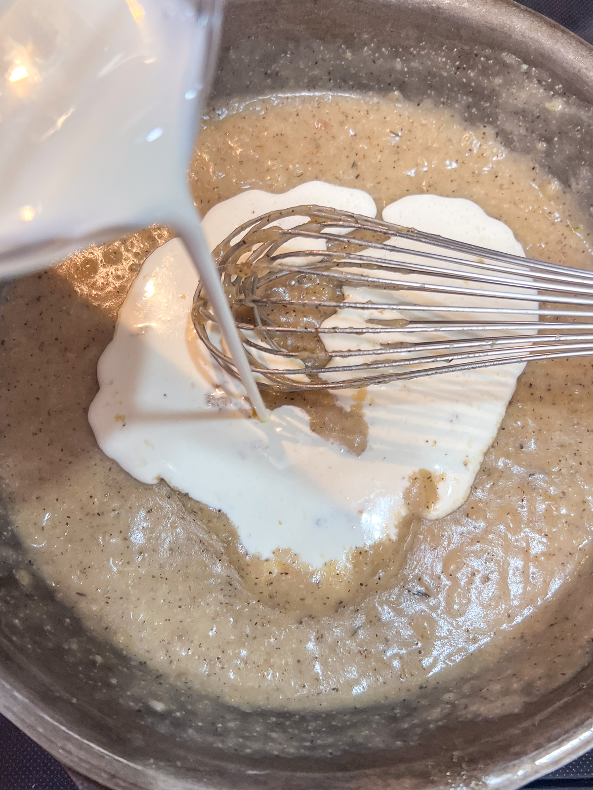 Heavy cream and chicken stock being whisked into the roux in a cast iron skillet.