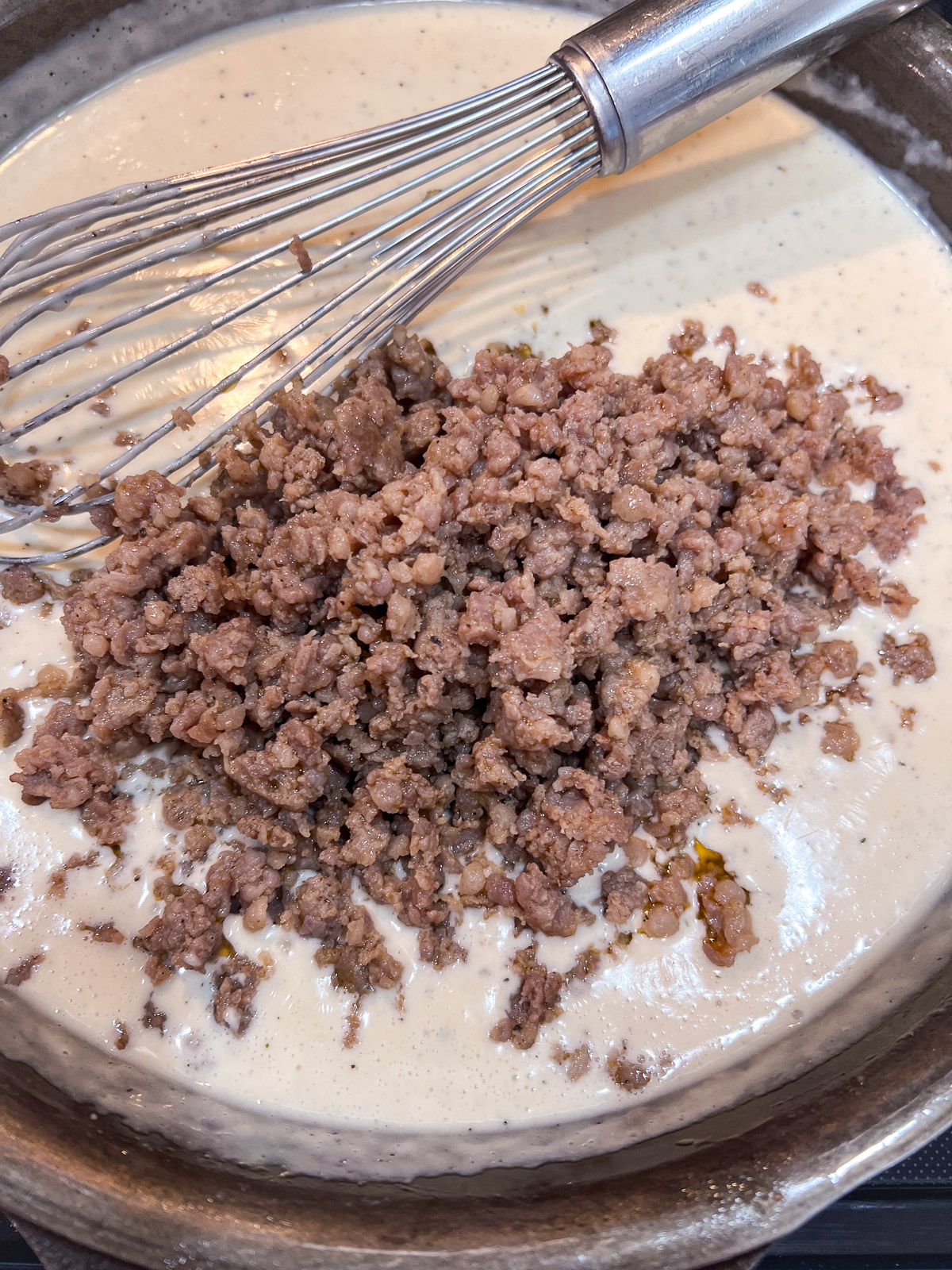 Breakfast sausage being added to the gravy in a cast iron skillet.
