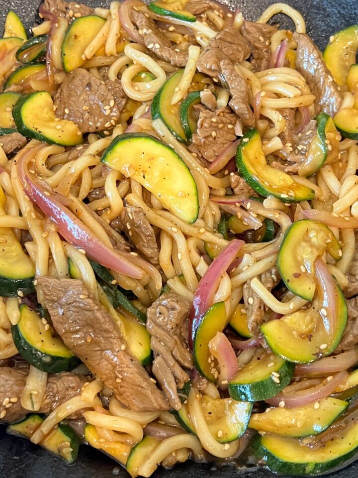 Teriyaki beef udon noodle stir fry finished in a cast iron wok.