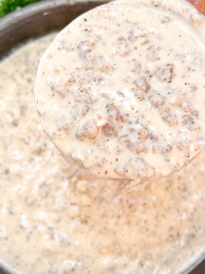 Creamy sausage gravy in a cast iron skillet with a spoonful lifted out