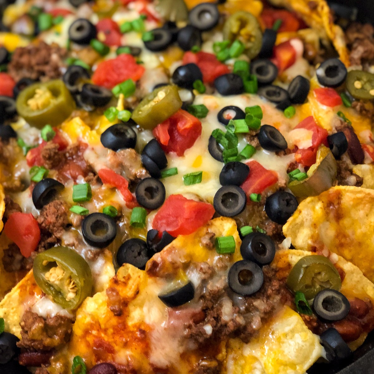 Loaded cast iron skillet nachos with jalapenos, black olives, tomatoes, and melted cheese