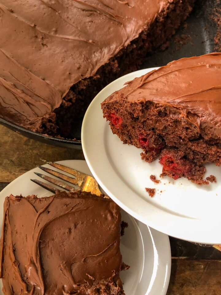 Cherry chocolate cake baked in a cast iron skillet with two frosted slices served on plates.