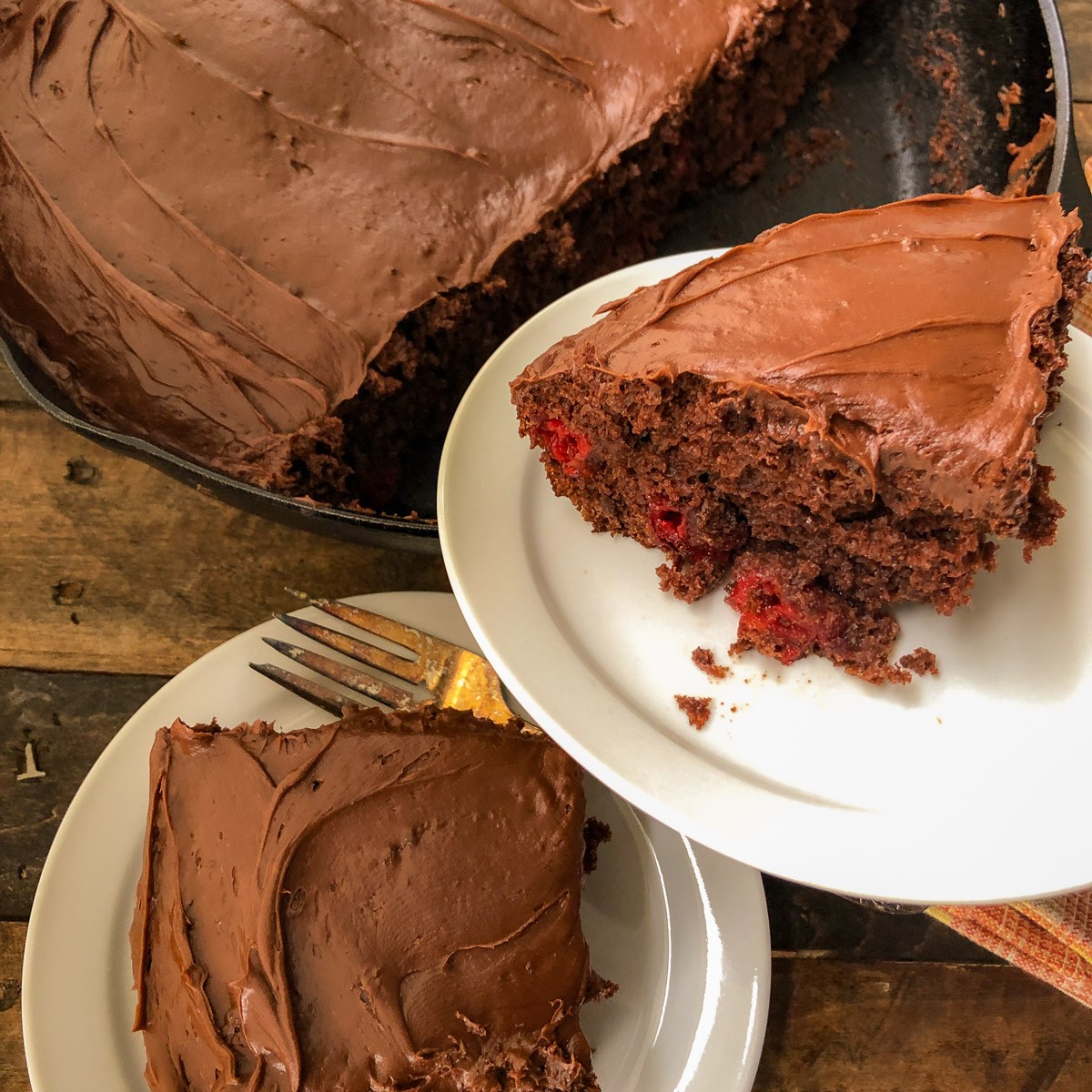 Cherry chocolate cake baked in a cast iron skillet with two frosted slices served on plates.
