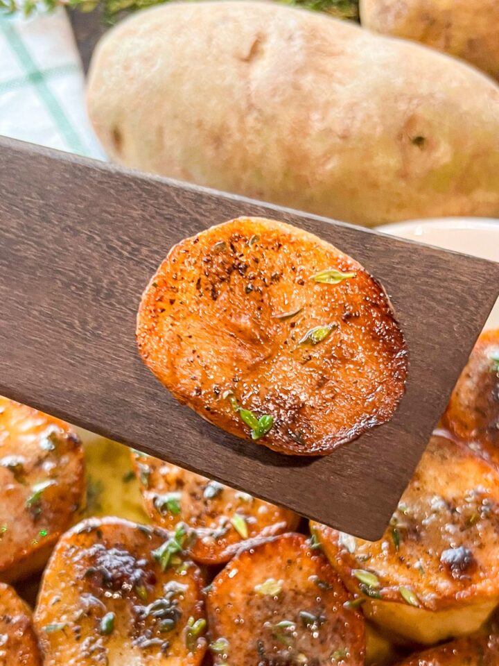 Fondant potatoes recipe with a single golden seared potato on a wooden spatula