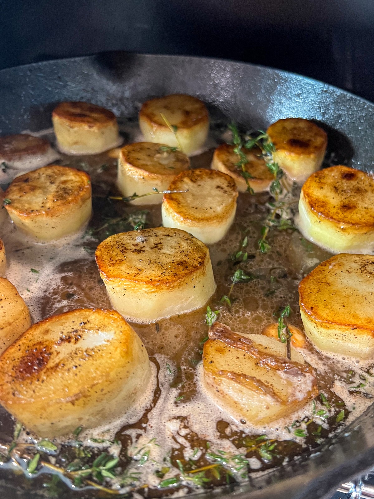 Seared potatoes in butter chicken stock with garlic and thyme is being placed in the oven.