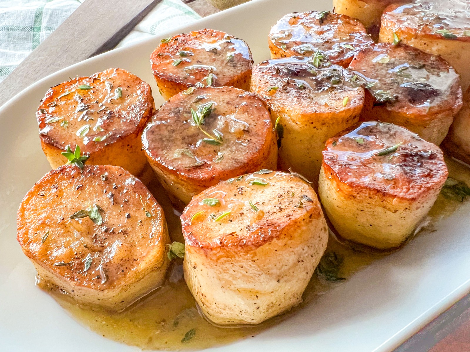 Freshly cooked potatoes on a white serving platter with the pan sauce poured over and pooling at the bottom.