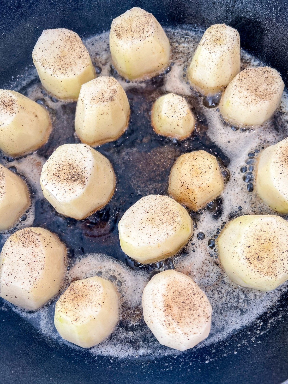 Seasoned potato discs in a searing hot cast iron skillet with melted butter and avocado oil.