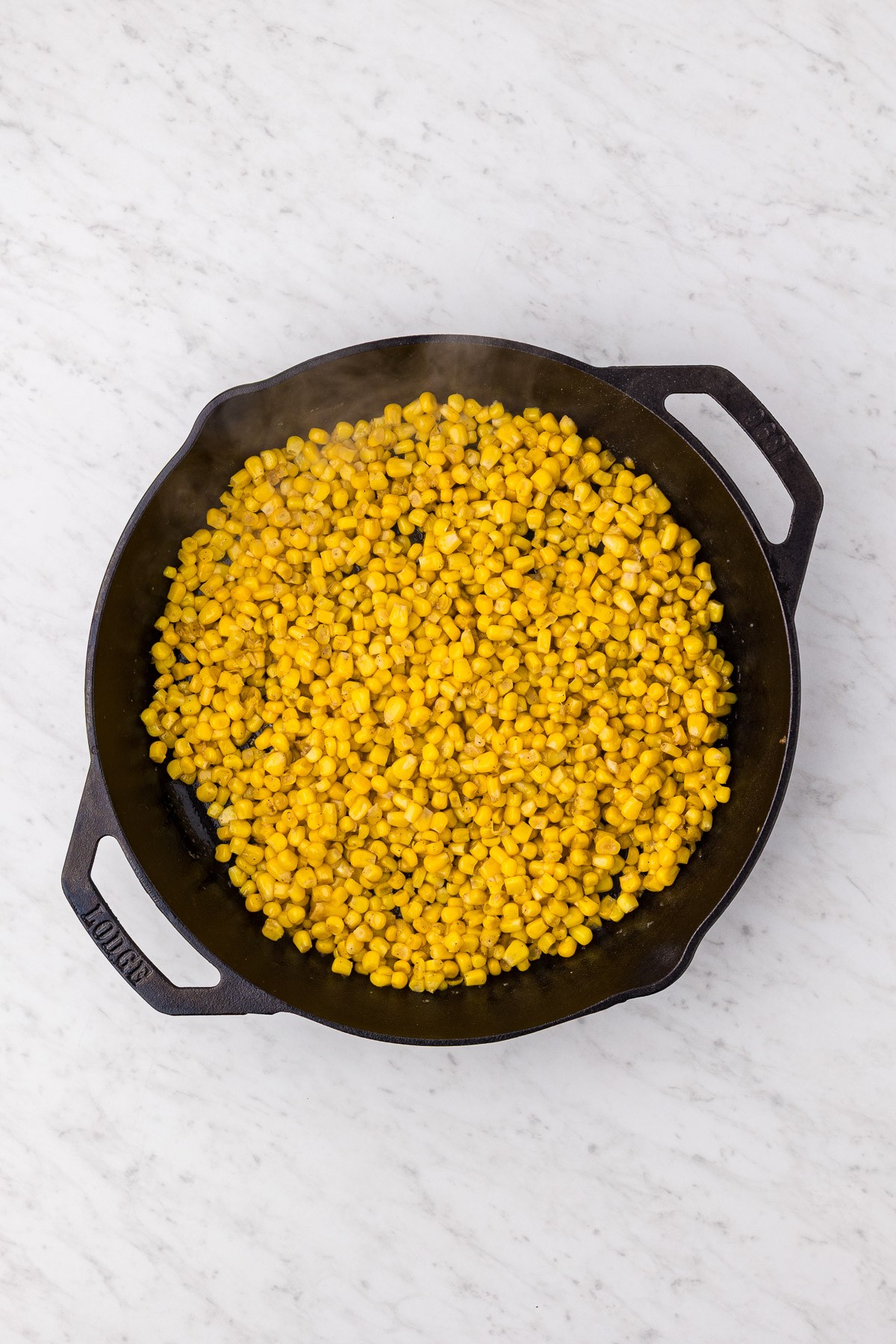 Drained corn kernels added to the garlic butter in a cast iron skillet