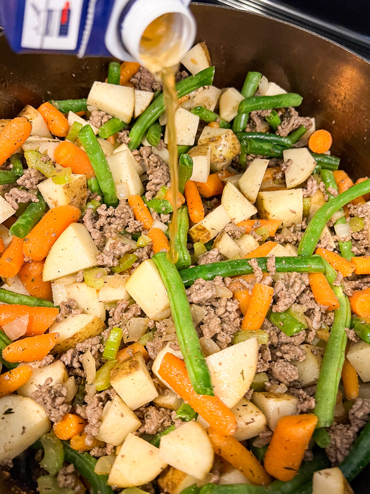 Broth being added to dutch oven of meat and vegetables.