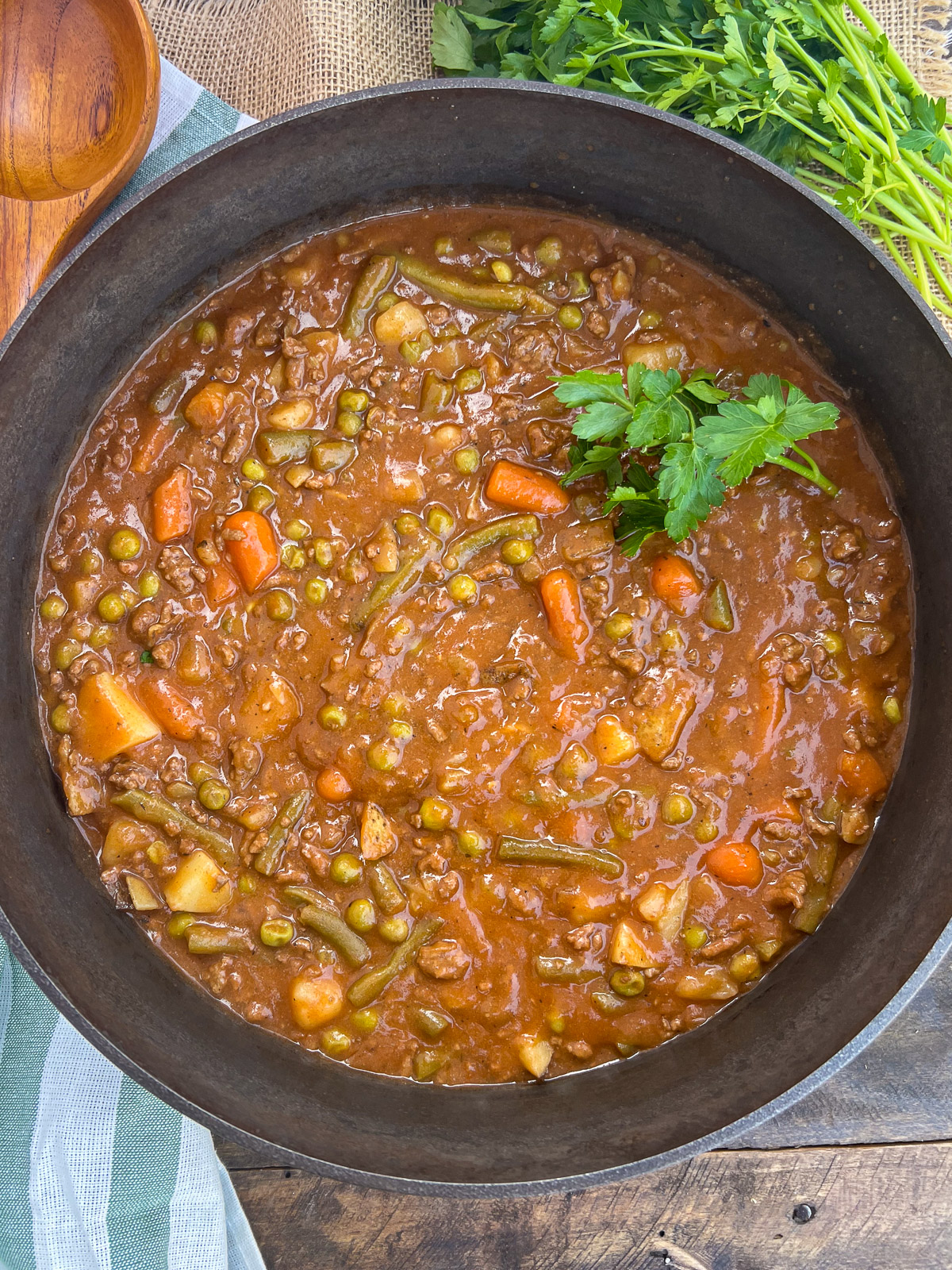 Dutch oven ground beef stew garnished with fresh parsley is ready to be served.