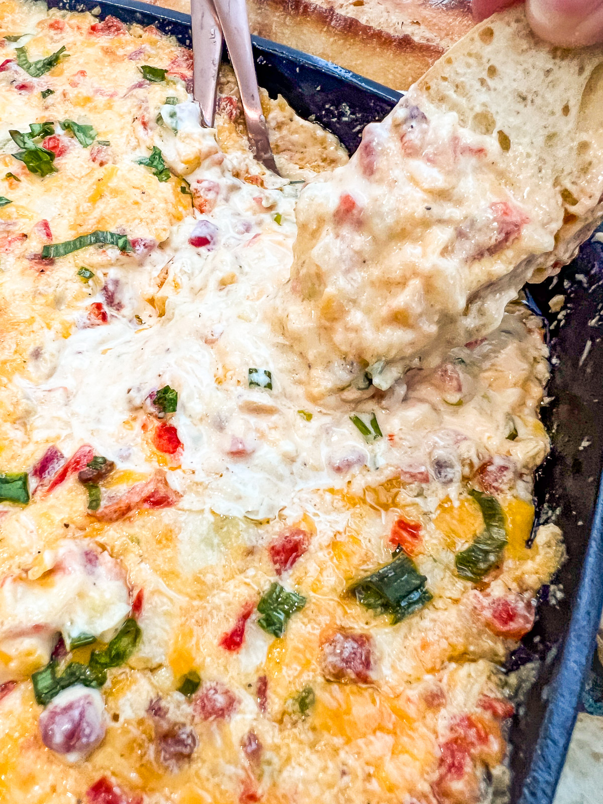 Baked pimento cheese dip in a cast iron skillet served with sliced baguette