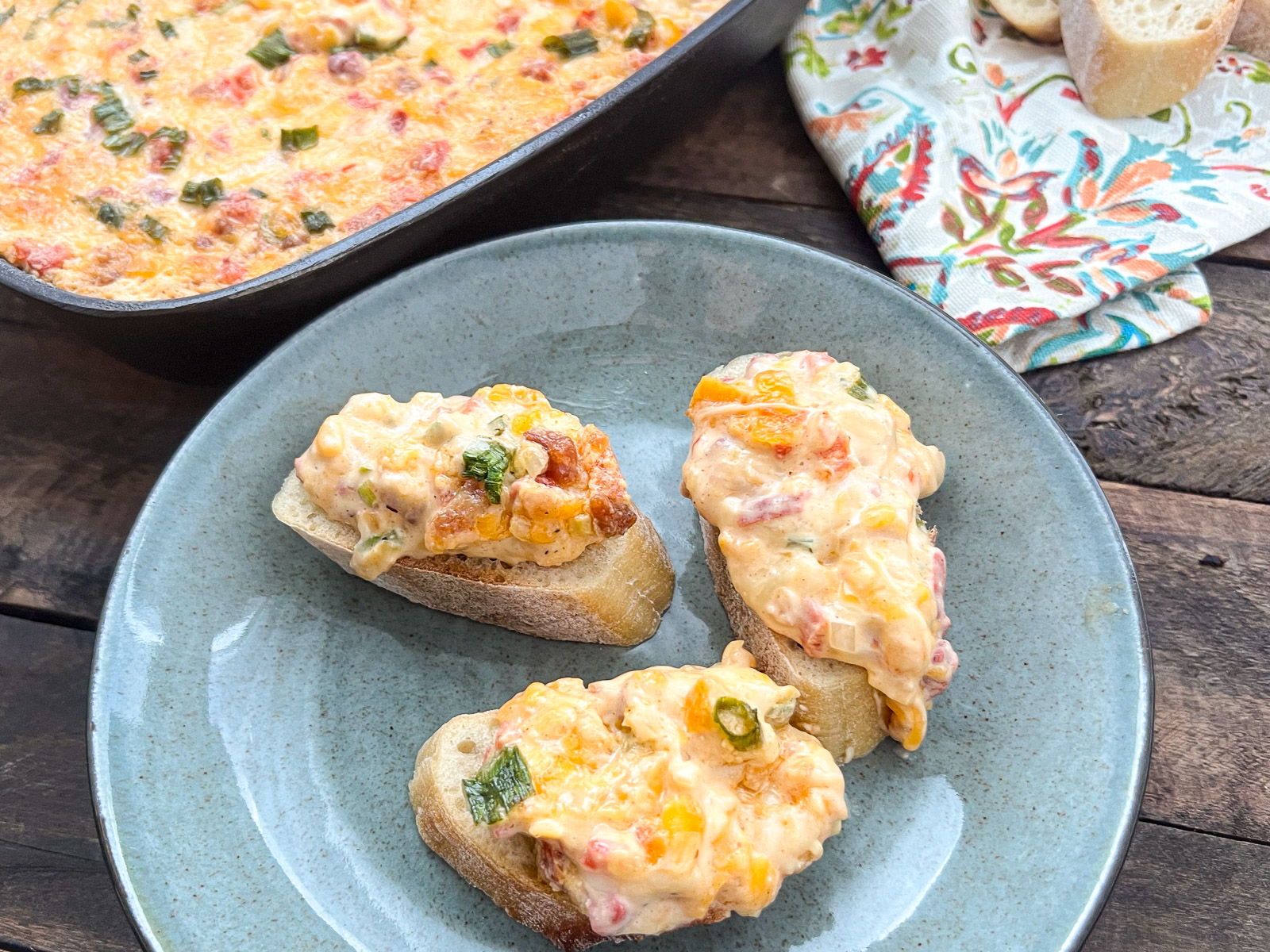 Slices of baguette topped with hot pimento cheese dip on a plate