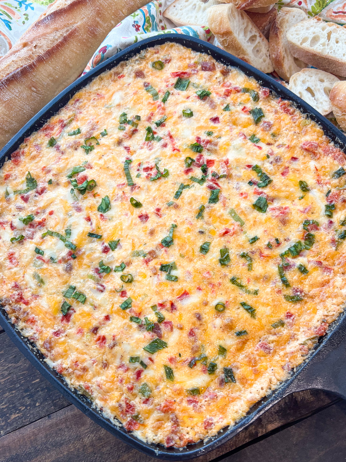 Pimento cheese dip spread in a cast iron skillet topped with green onions ready to bake