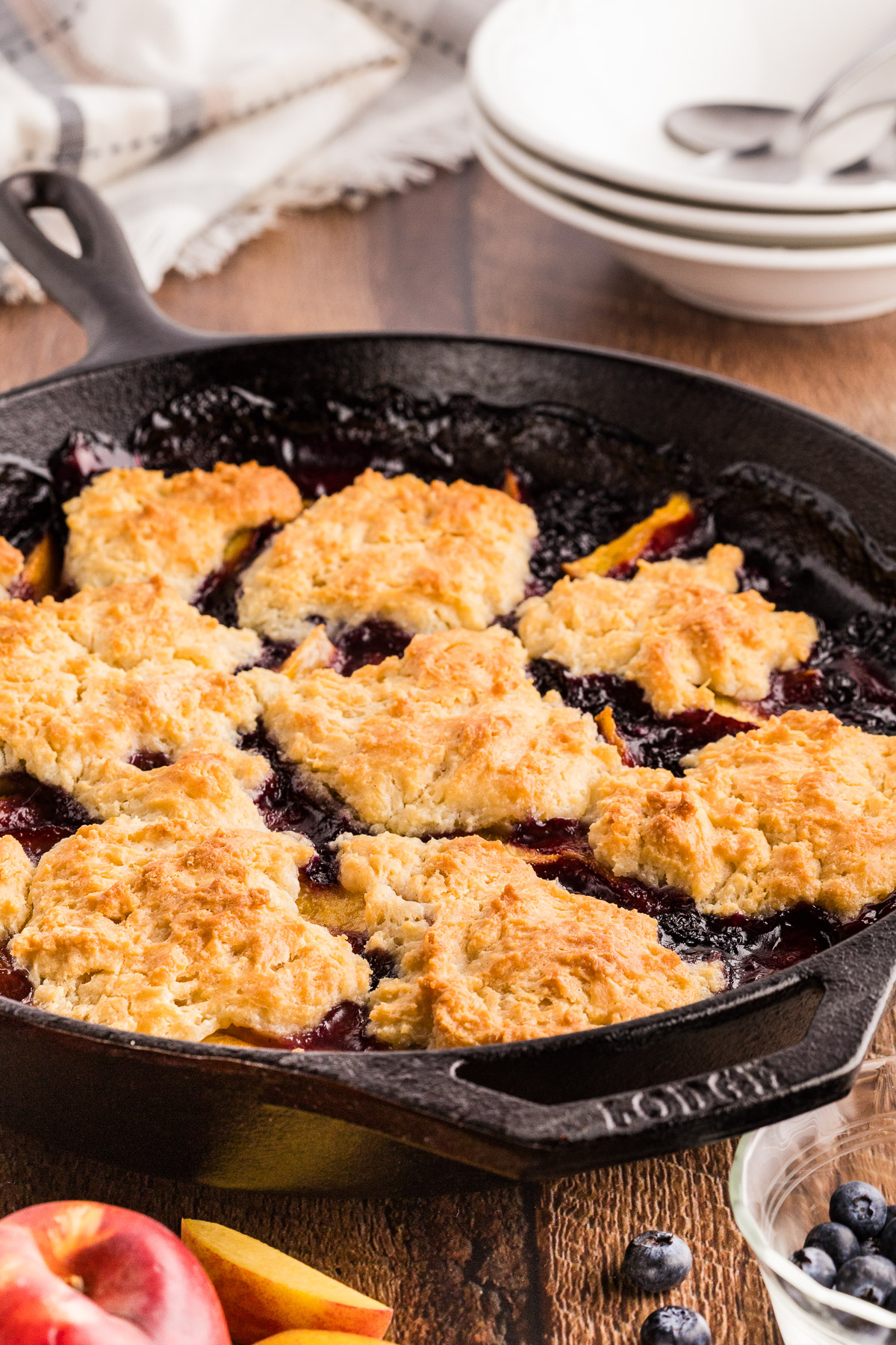 Peach blueberry cobbler in a cast iron skillet with plates and fresh fruit