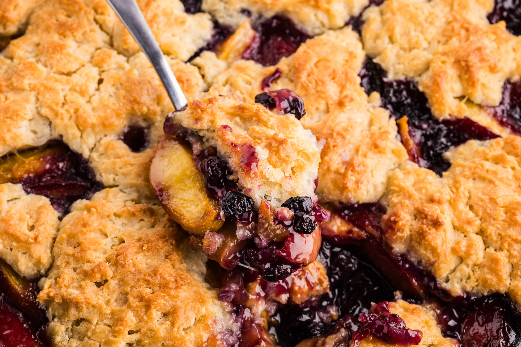 Spoon scooping peach blueberry cobbler from a cast iron skillet