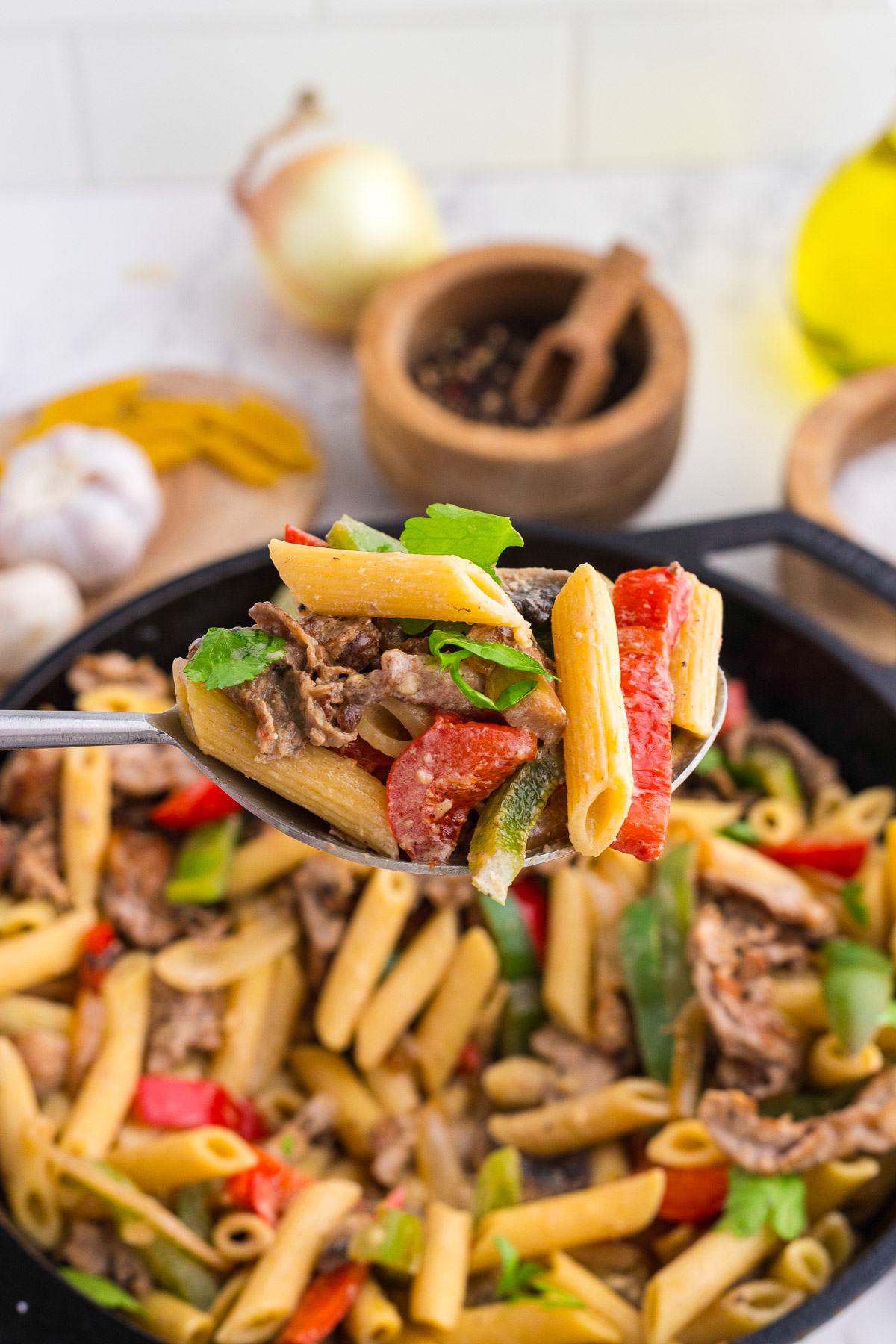 A spoonful of creamy philly cheesesteak pasta lifted from the cast iron skillet