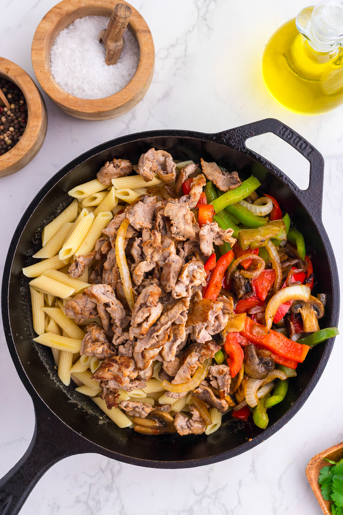 Penne pasta, seared beef, and sauteed vegetables combined in a cast iron skillet