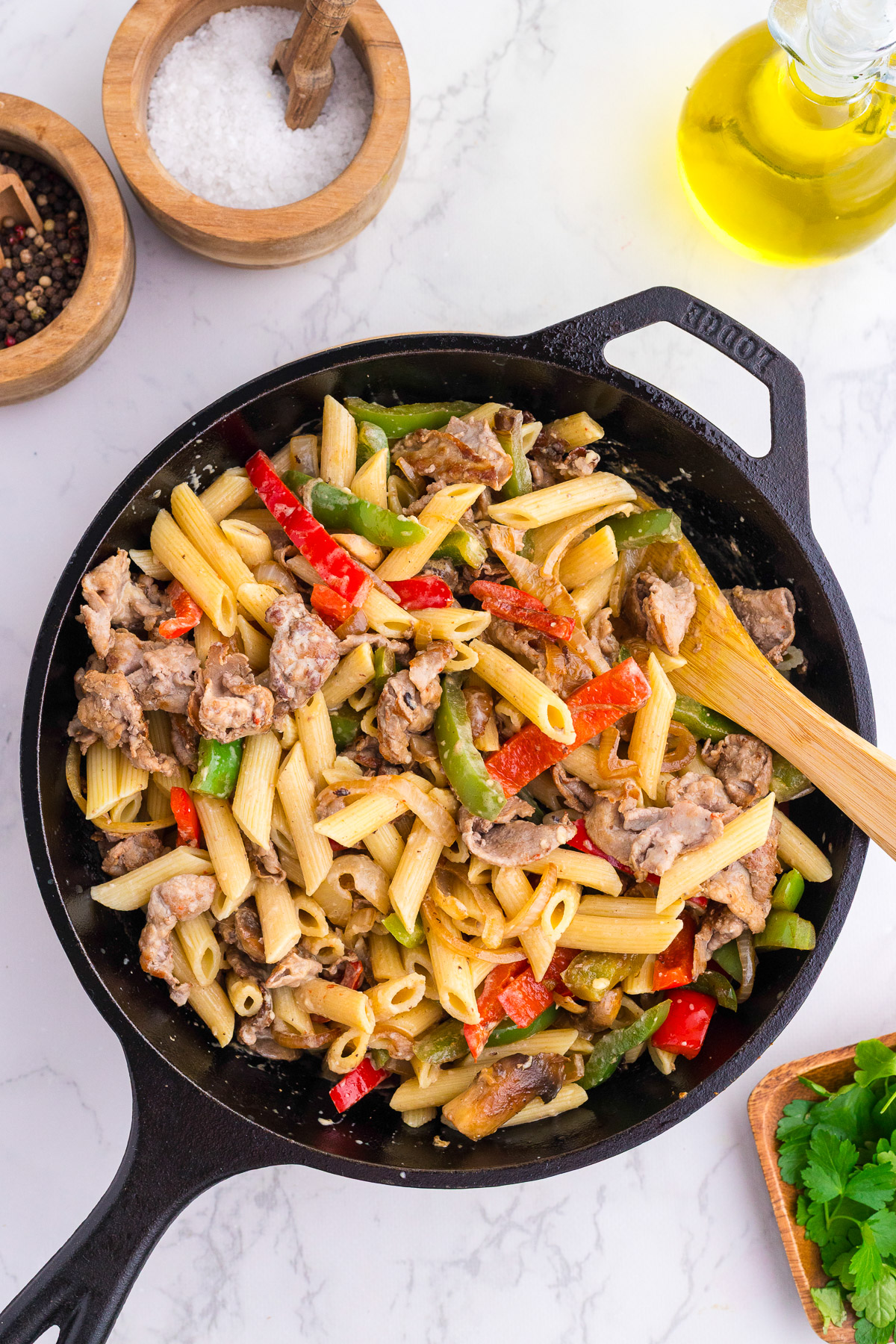 Philly cheesesteak pasta tossed together with a wooden spoon in a cast iron skillet