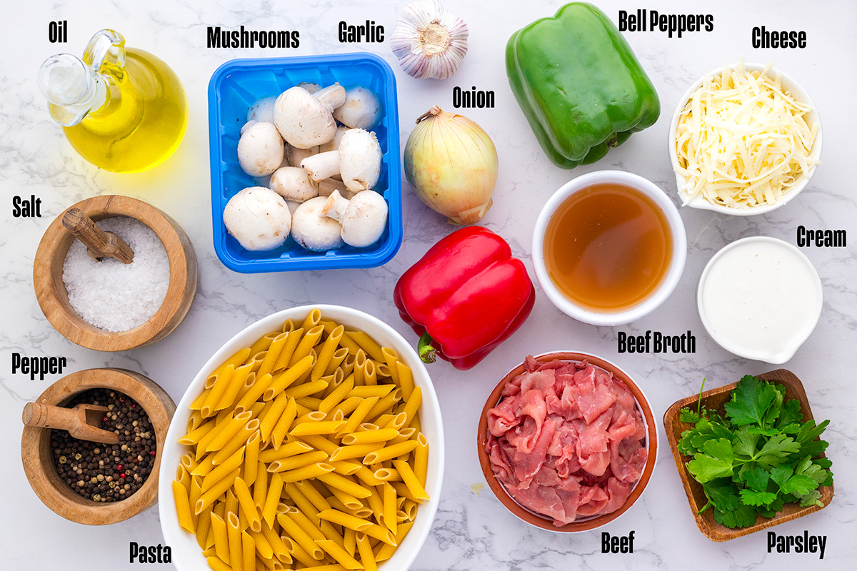 Ingredients for philly cheesesteak pasta laid out on a marble counter
