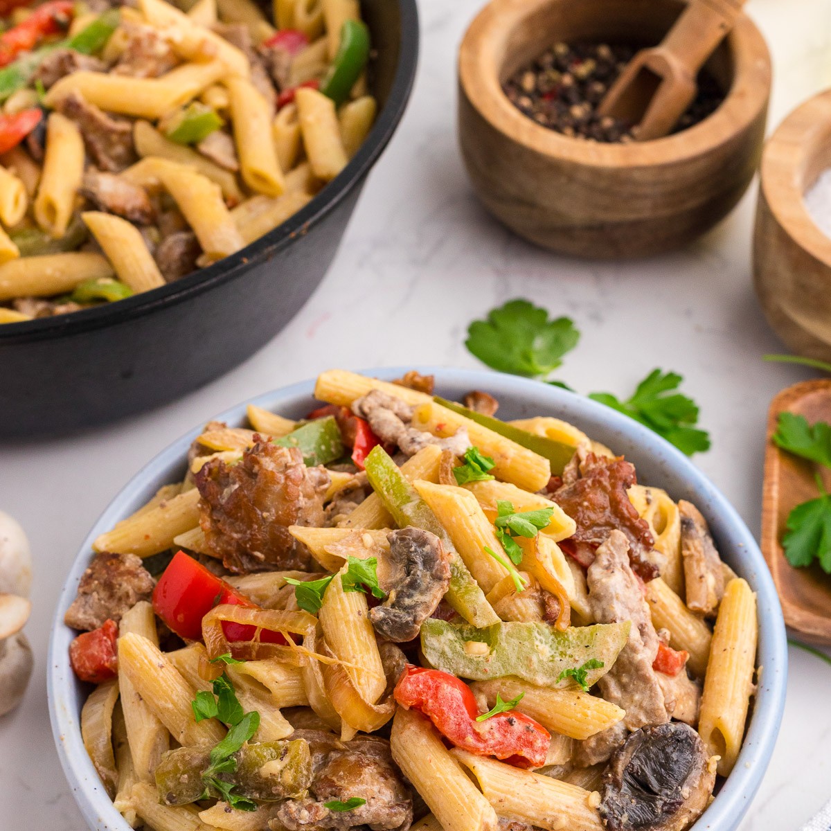 Philly cheesesteak pasta served in a blue bowl with parsley garnish