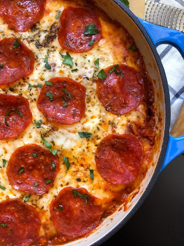 Pizza pasta bake with melted mozzarella and pepperoni in a blue Dutch oven.