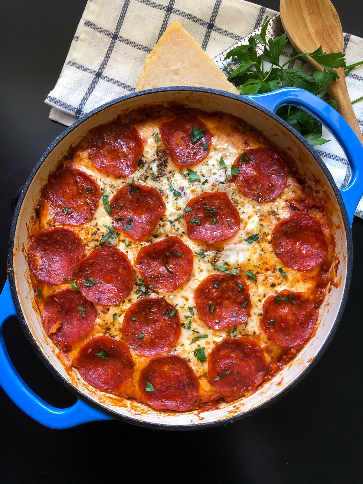 Overhead view of pizza pasta bake in a blue Dutch oven topped with pepperoni and fresh parsley.