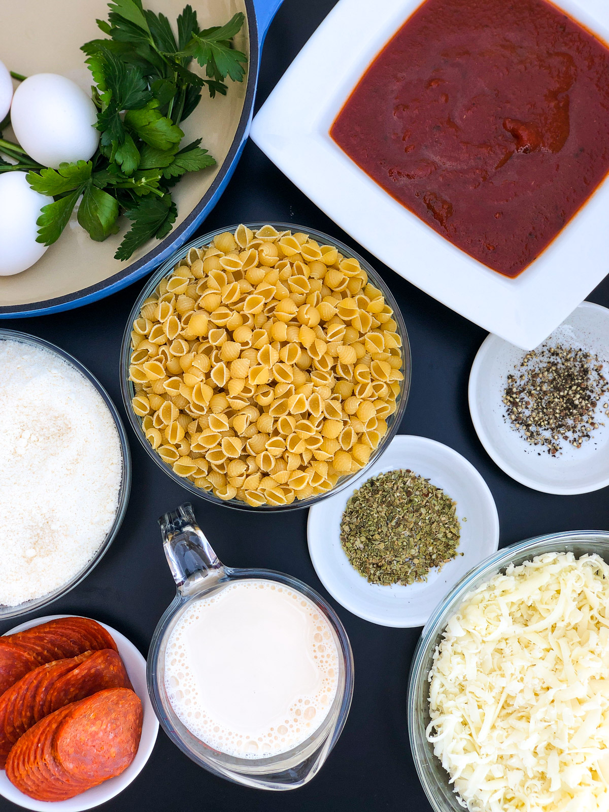 Ingredients for pizza pasta bake: shell pasta, pizza sauce, mozzarella, Parmesan, pepperoni, eggs, evaporated milk, oregano, black pepper, and parsley.
