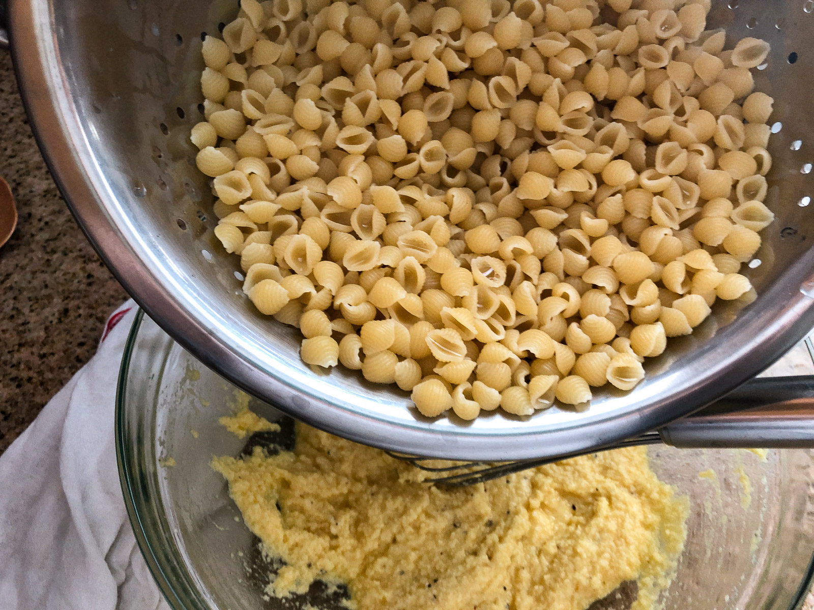 Adding drained shell pasta to the egg and cheese mixture in a glass bowl.