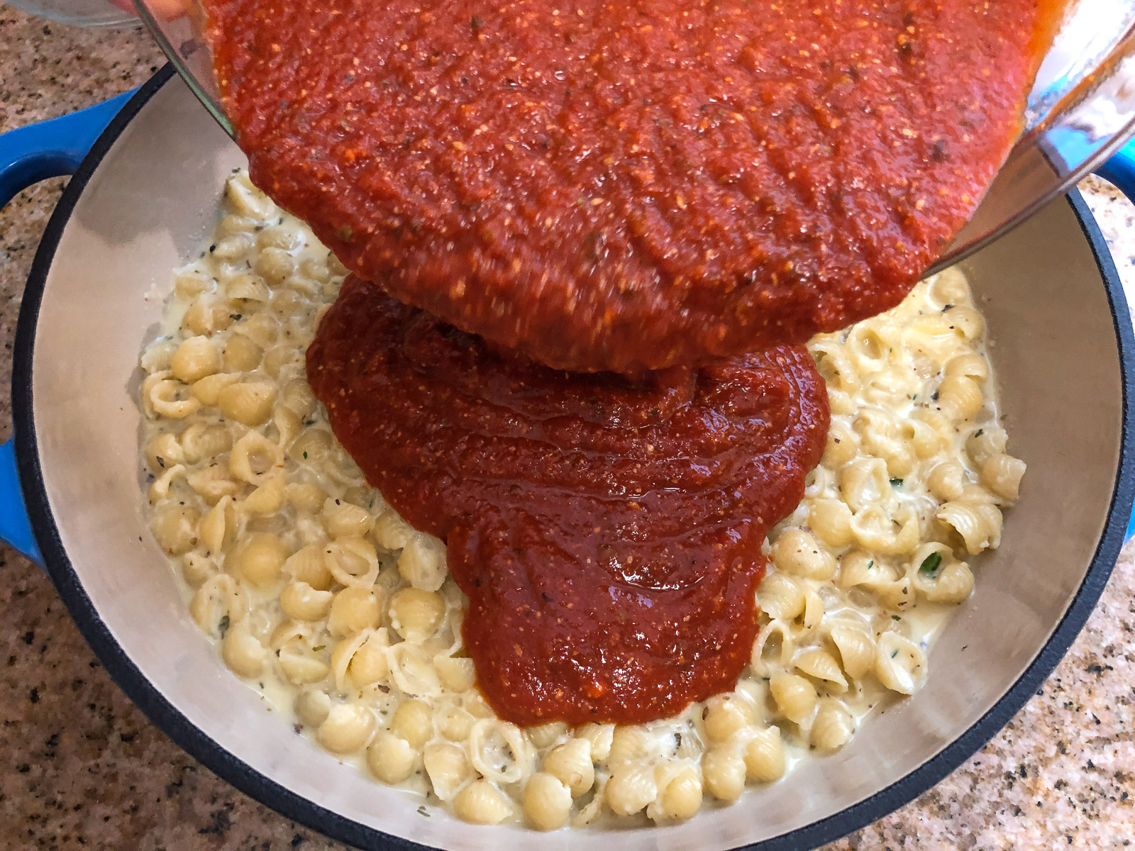 Pouring seasoned pizza sauce over the pasta layer in the Dutch oven.